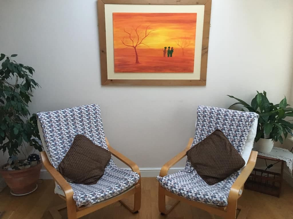 Therapy room – Hypnotherapist Newcastle Two cushioned chairs facing each other beneath a sunset painting in the therapy room